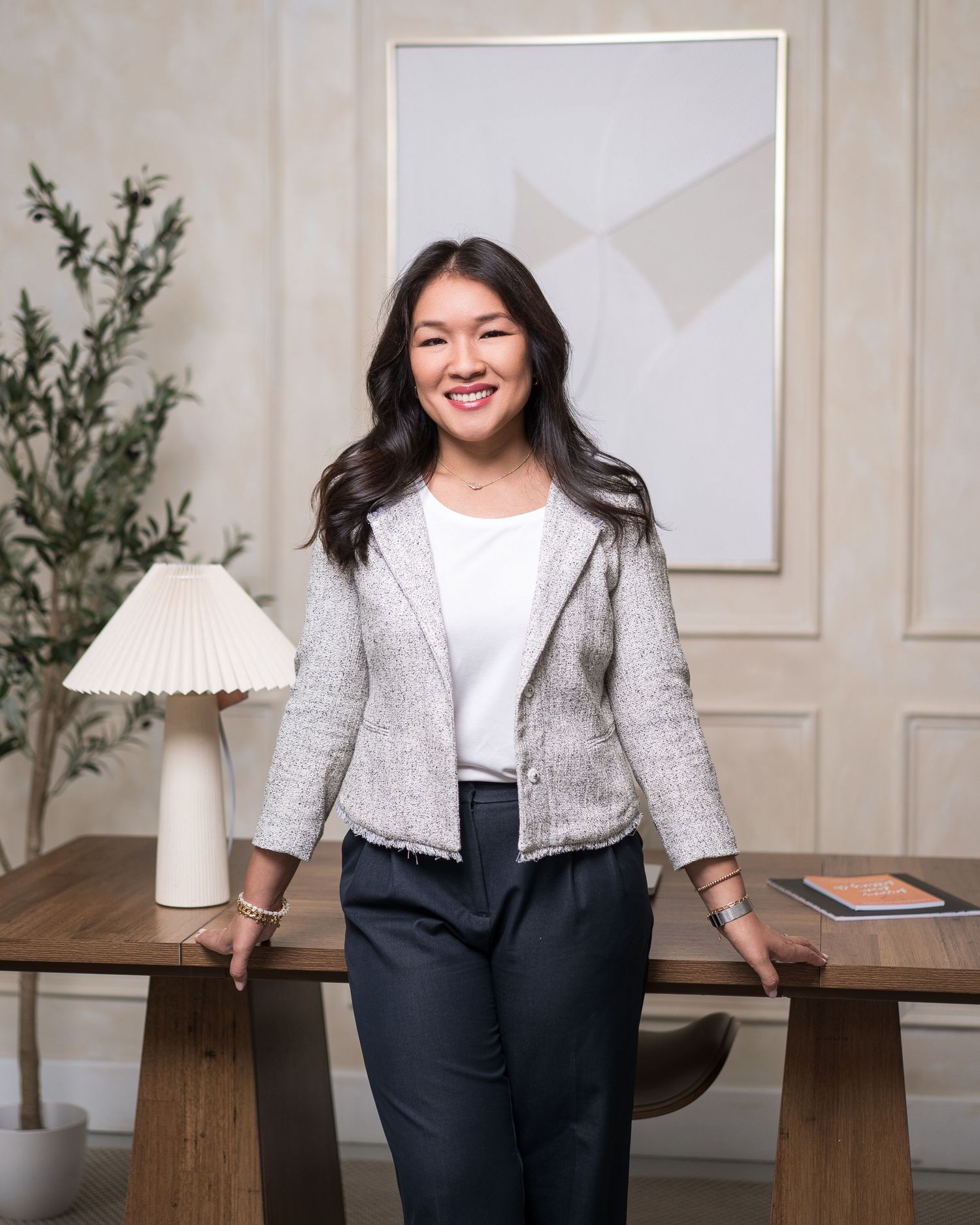 Woman in gray cardigan and dark pants standing by wooden table in minimalist room.