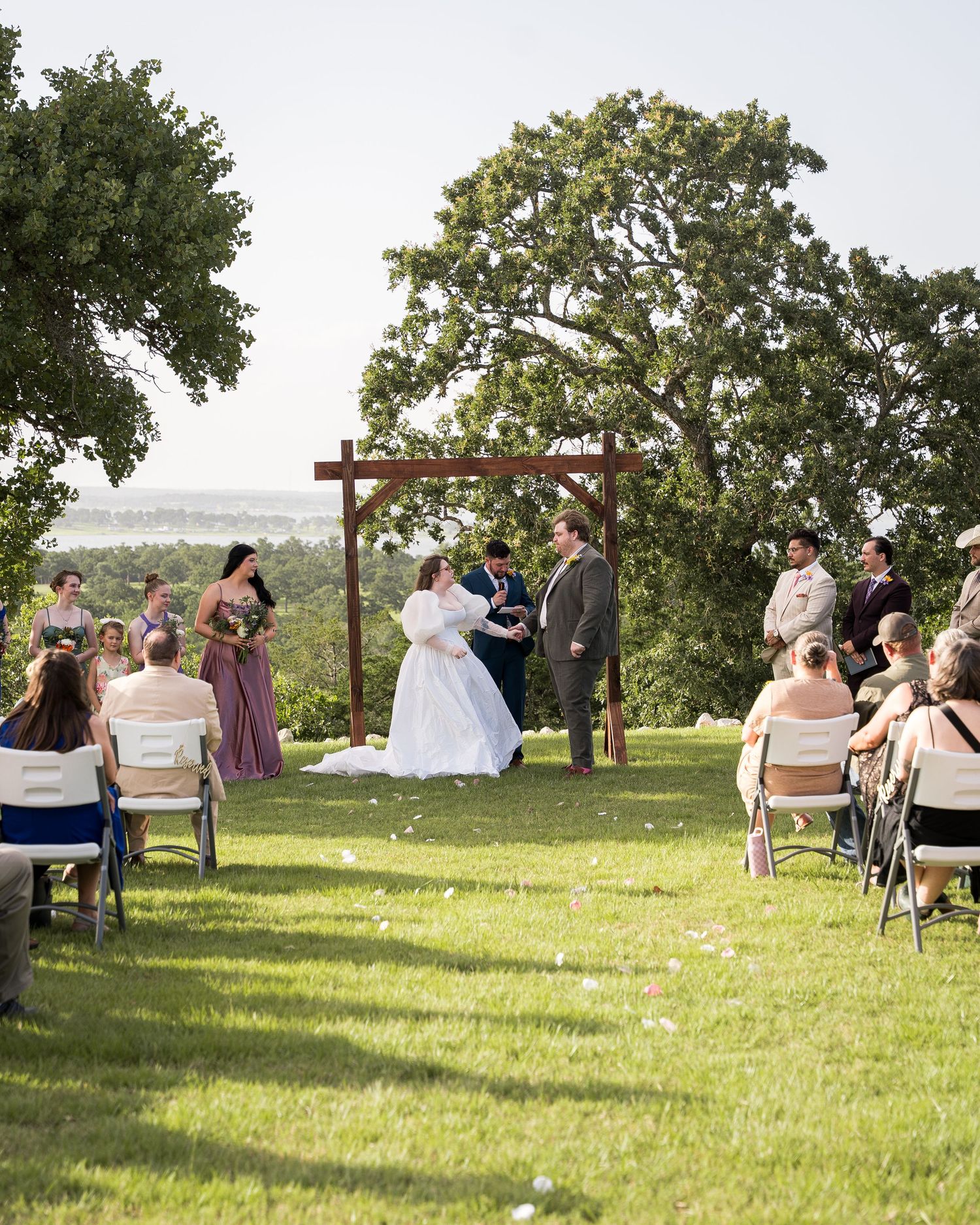 A bride and groom exchange vows under a wooden cross arch on a scenic hilltop outdoor wedding ceremony.
