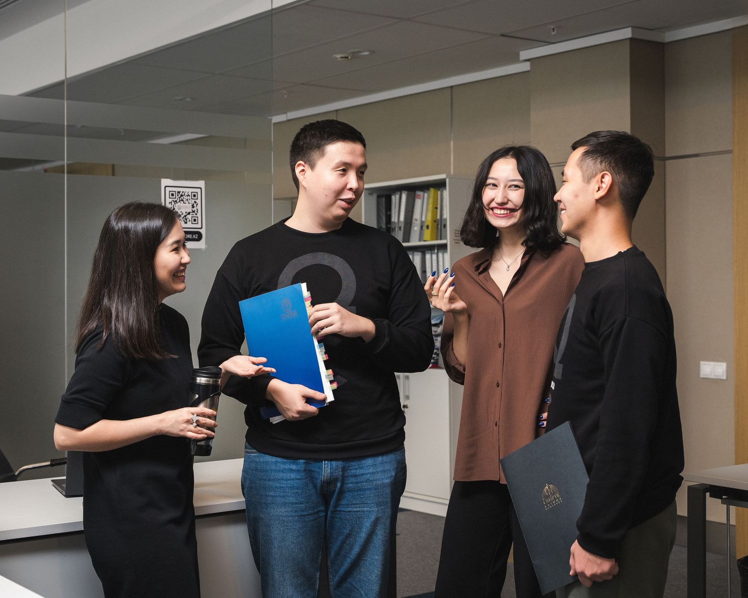 Group of professionals discussing project details while holding folder in office hallway.
