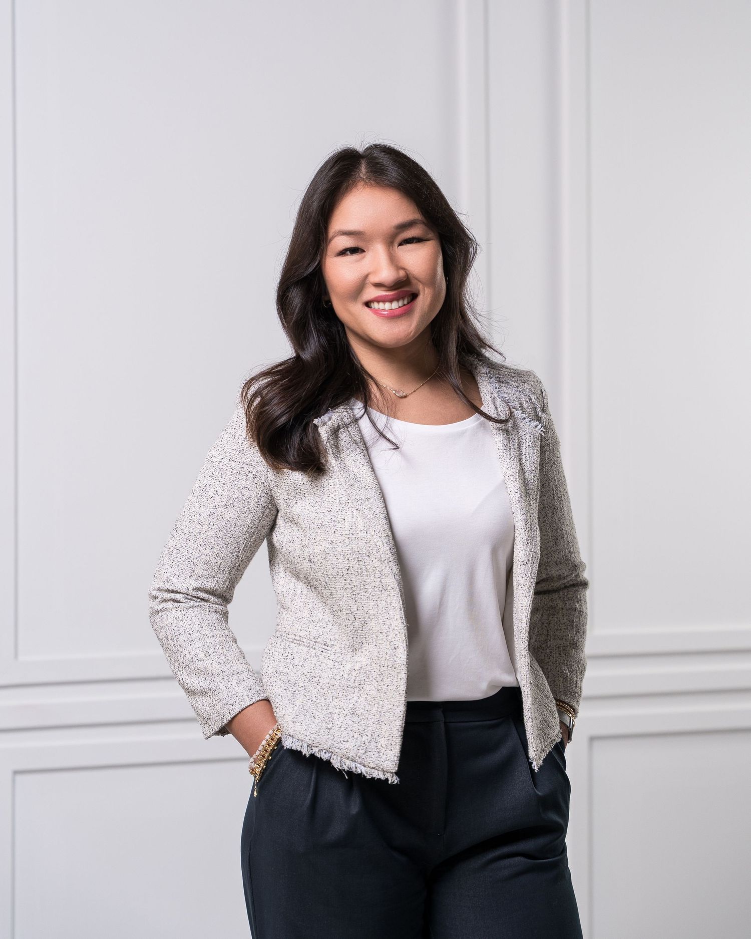 Professional in gray blazer and white top posing against white wall background.