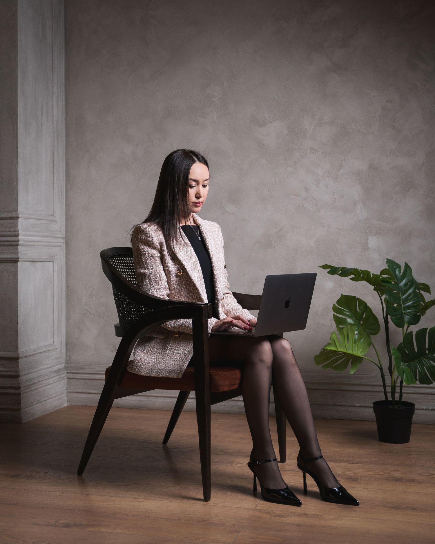 Professional working on laptop while seated in modern grey chair with plants in background.