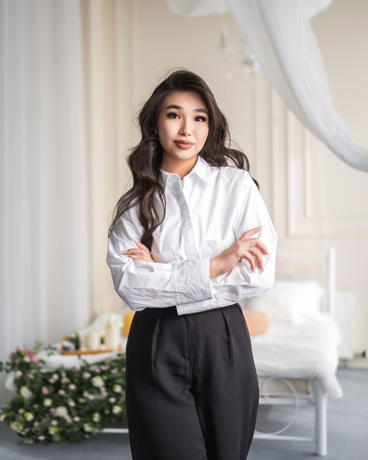 Person in white blouse and black pants posing elegantly in bright interior setting.