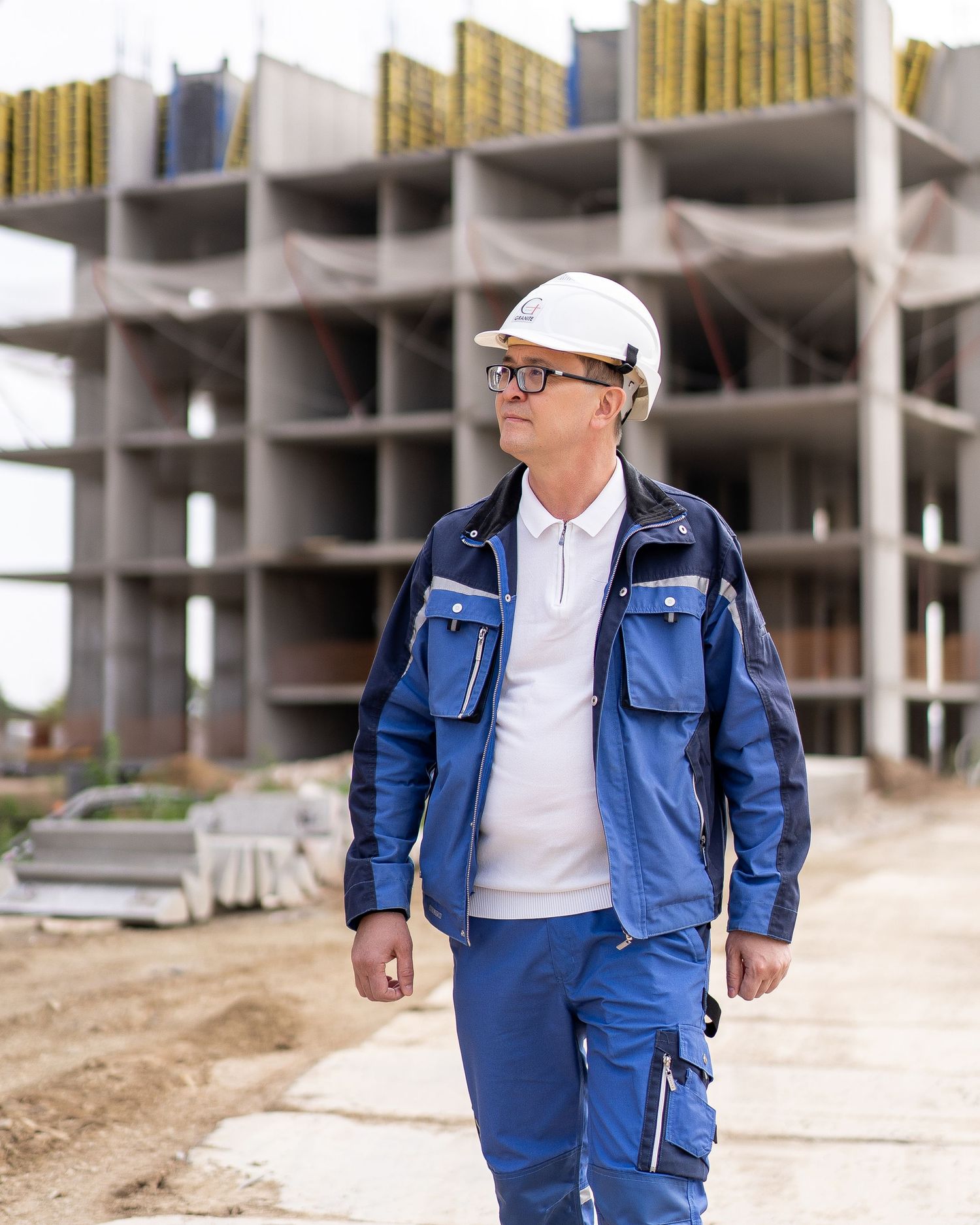 Worker in blue protective workwear and white hardhat walking at construction site.