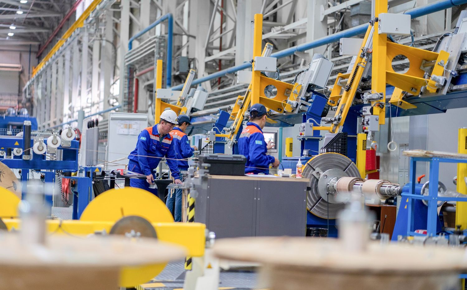 Factory workers in blue uniforms operating industrial machinery on production line.
