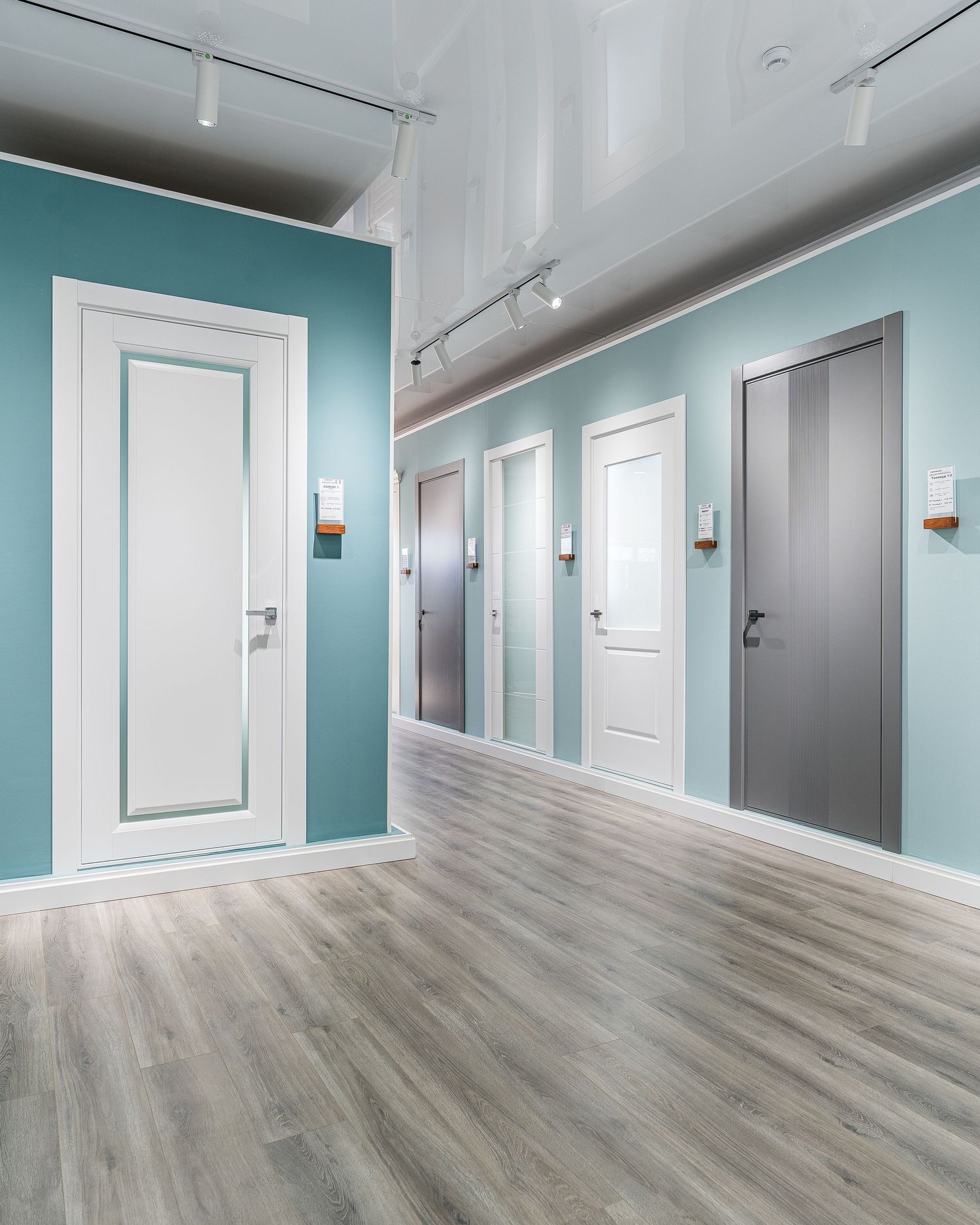 Commercial hallway featuring light wood flooring, turquoise walls, and multiple white doors.