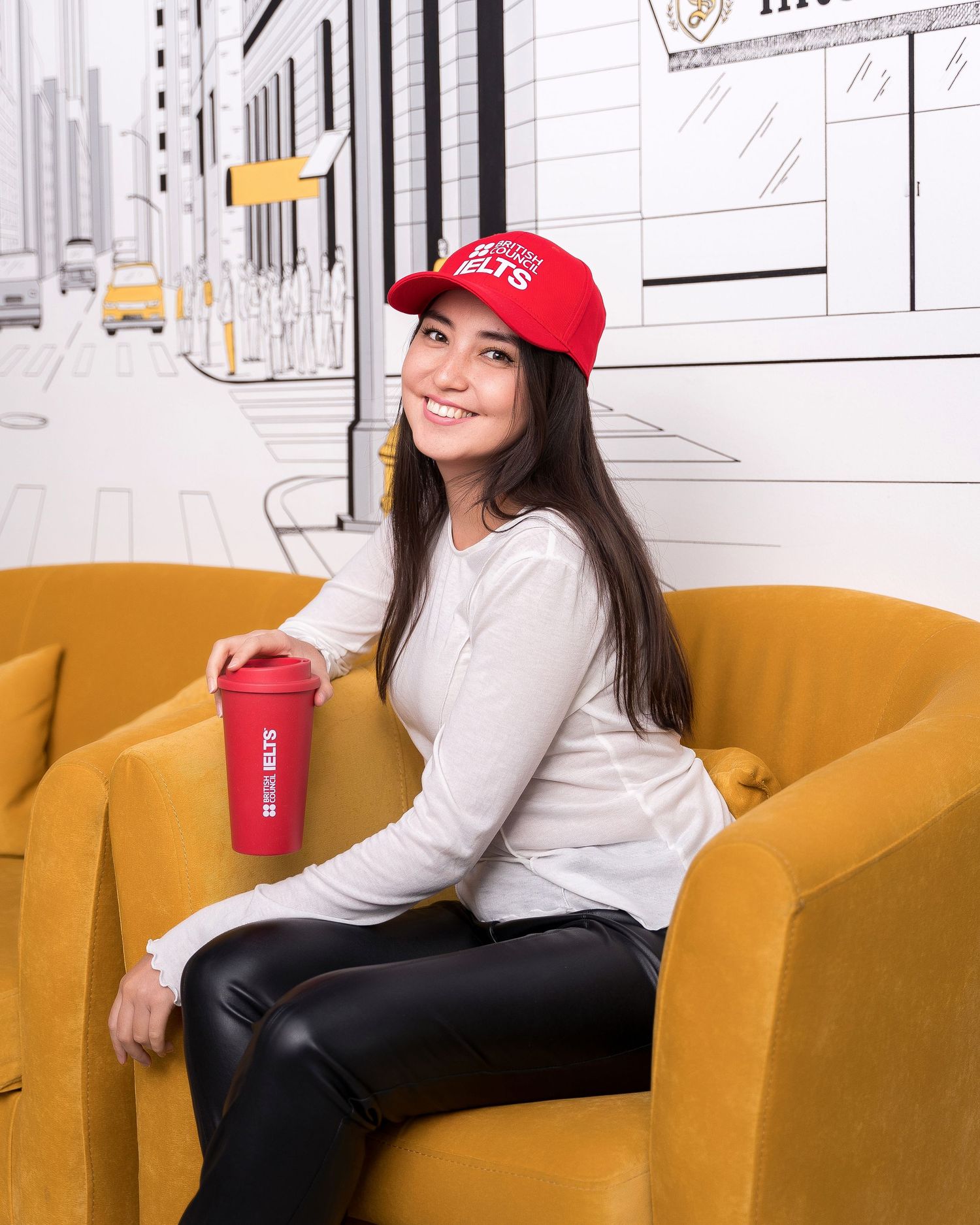 Student relaxing on yellow armchair with red coffee cup in modern study space.