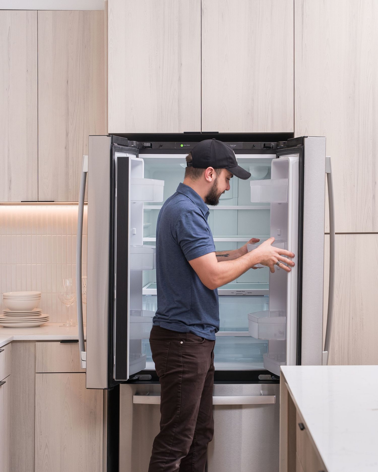Technician inspecting and servicing a modern stainless steel refrigerator in luxury kitchen.
