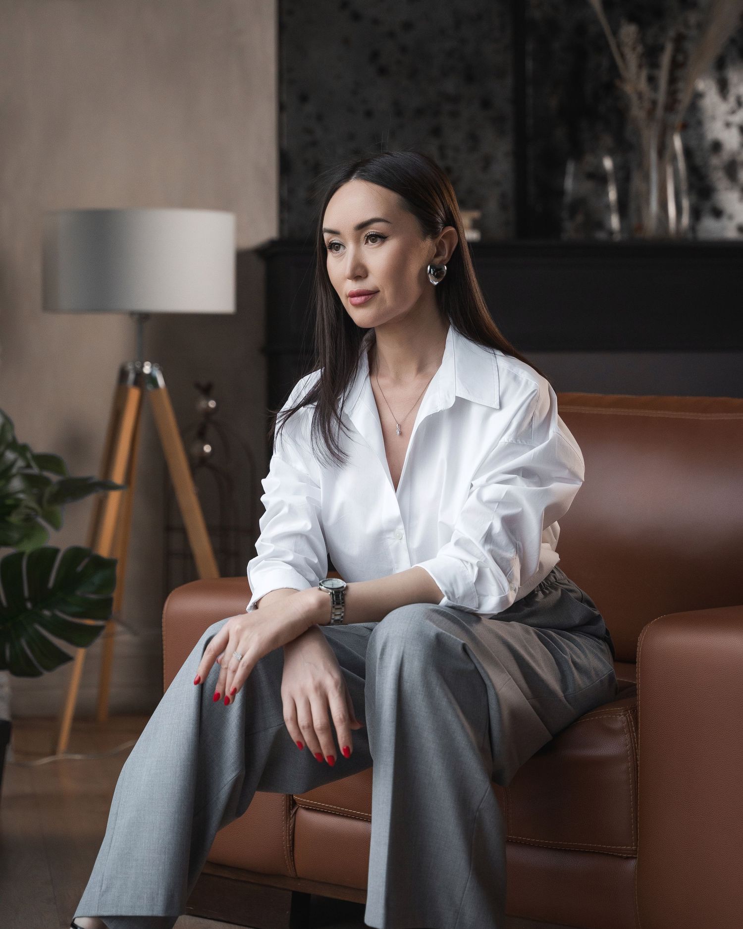 Professional in white shirt and grey pants seated on brown leather couch.