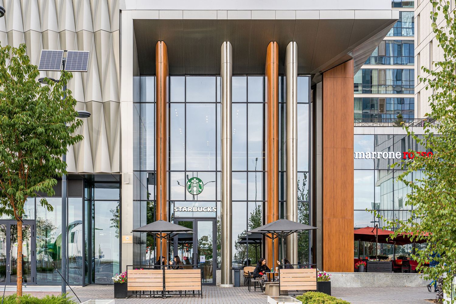 Glass and metal building facade with geometric patterns and outdoor seating area.