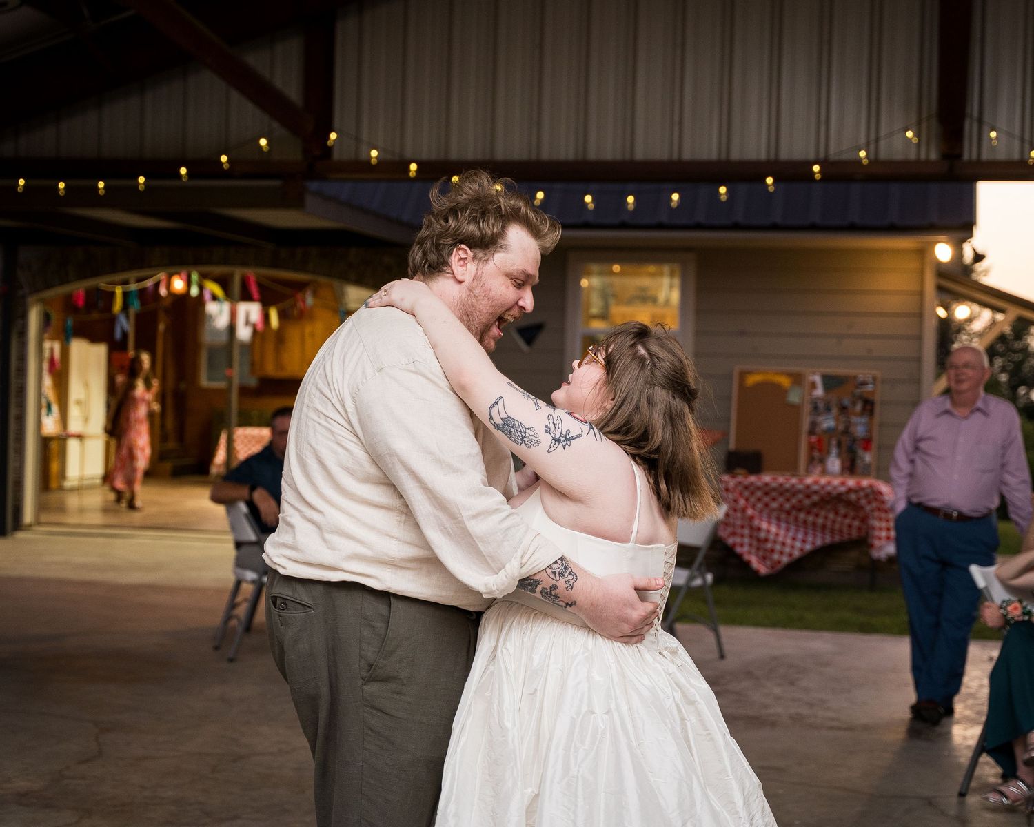 Couple shares first dance at rustic outdoor wedding reception with string lights and barn backdrop.