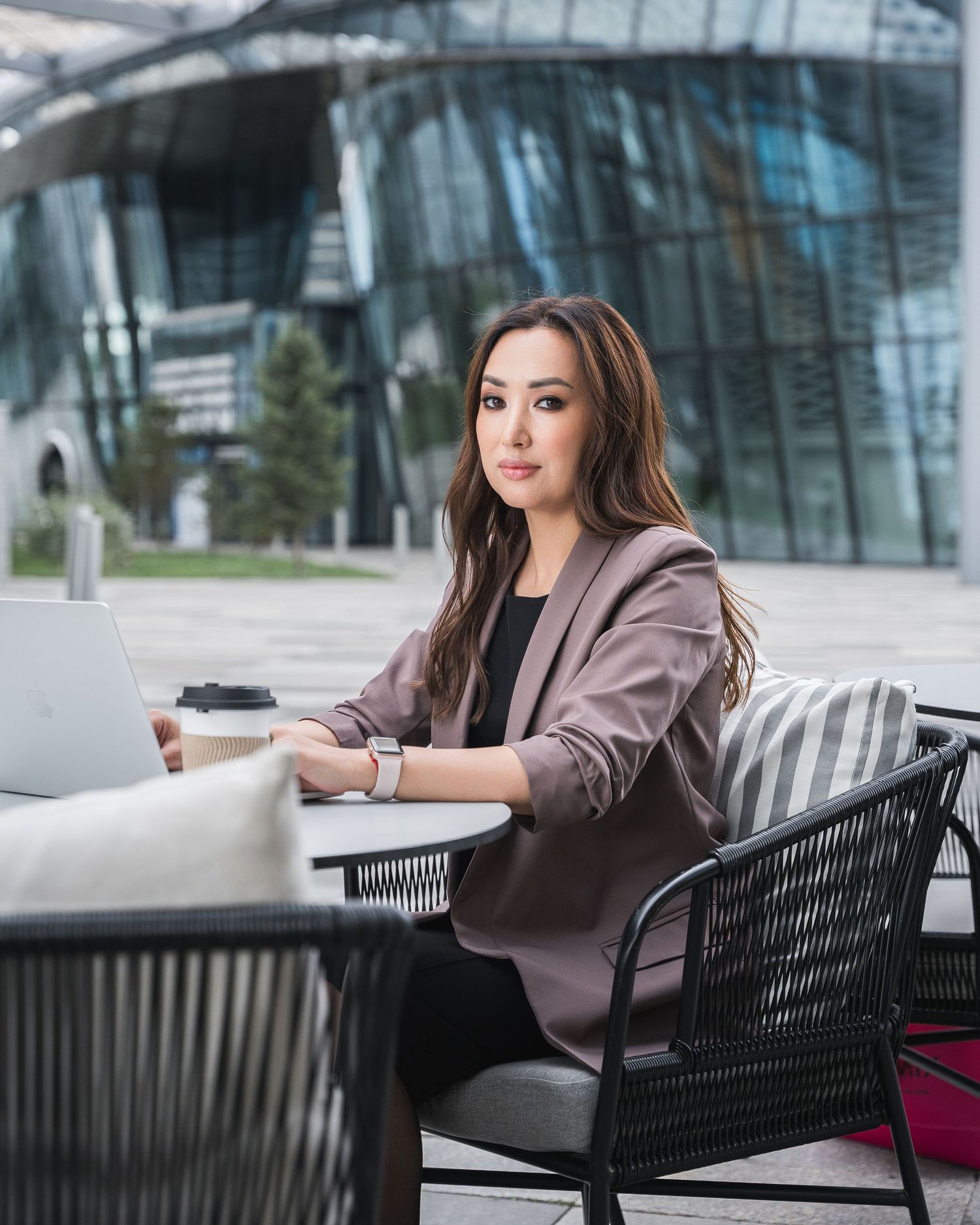 Professional woman in brown blazer working at outdoor cafe table with laptop and phone.