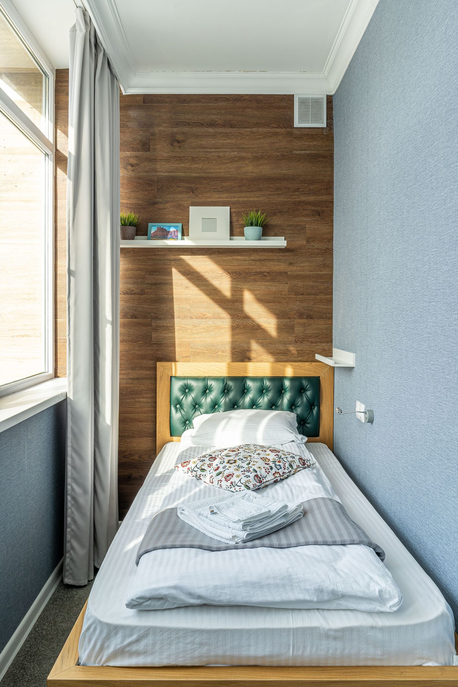 Contemporary bedroom design featuring wood accent wall and tufted green headboard with natural lighting.