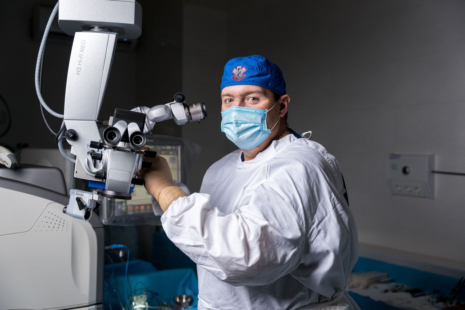 Medical specialist performing delicate procedure using microscope equipment in dimly lit room.