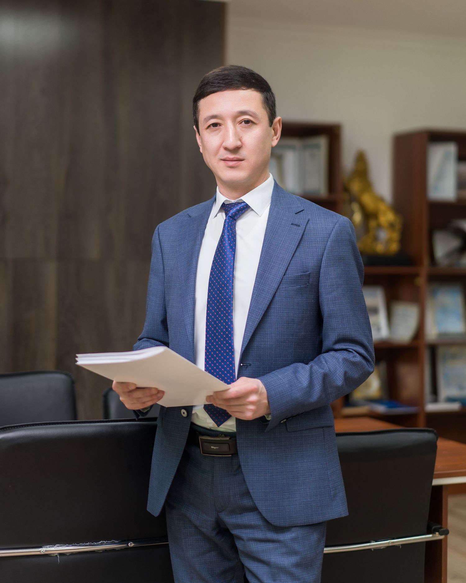 Professional in a blue suit and tie reviews documents while standing in an office setting.