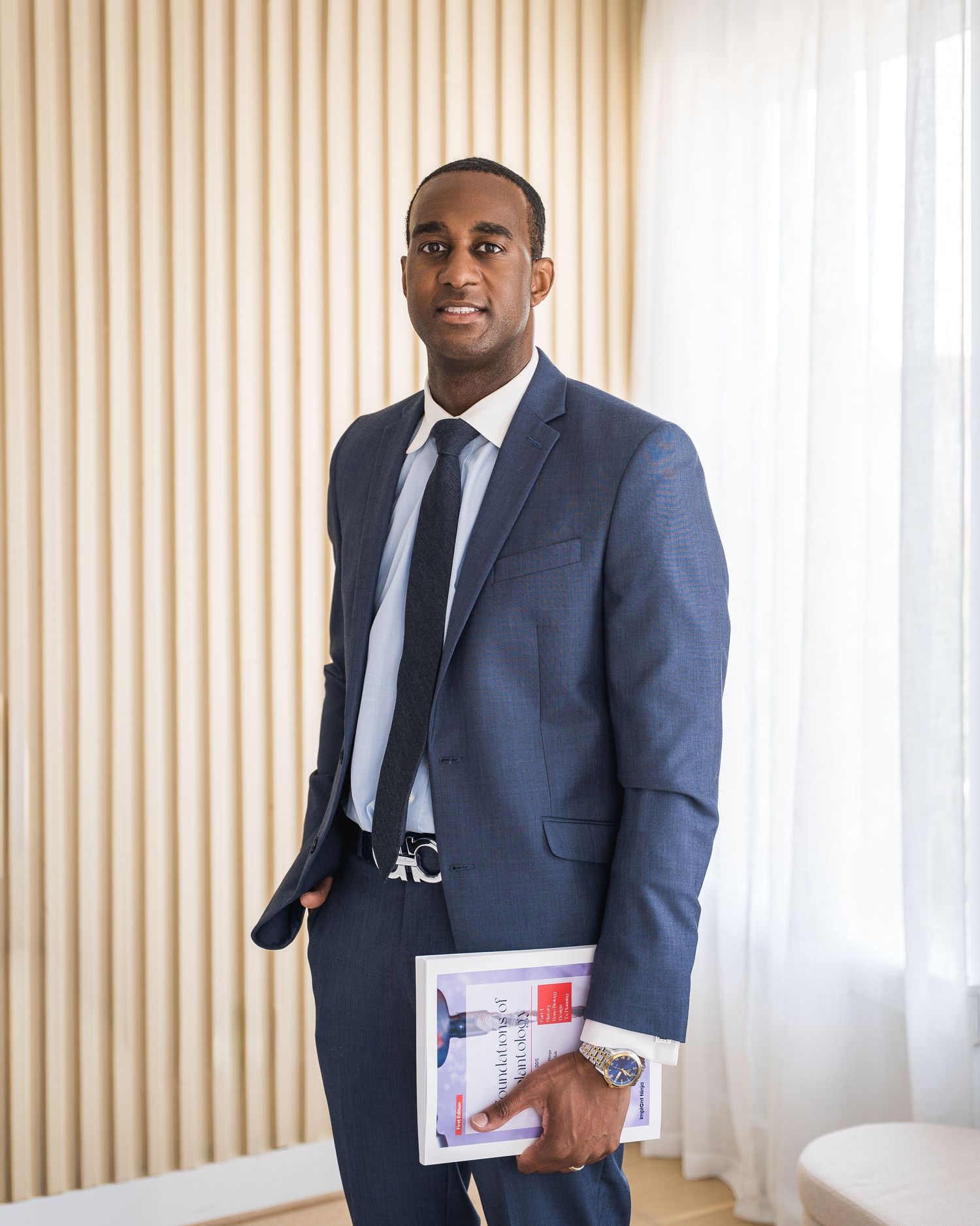 Professional in navy suit holding documents against striped wall background.