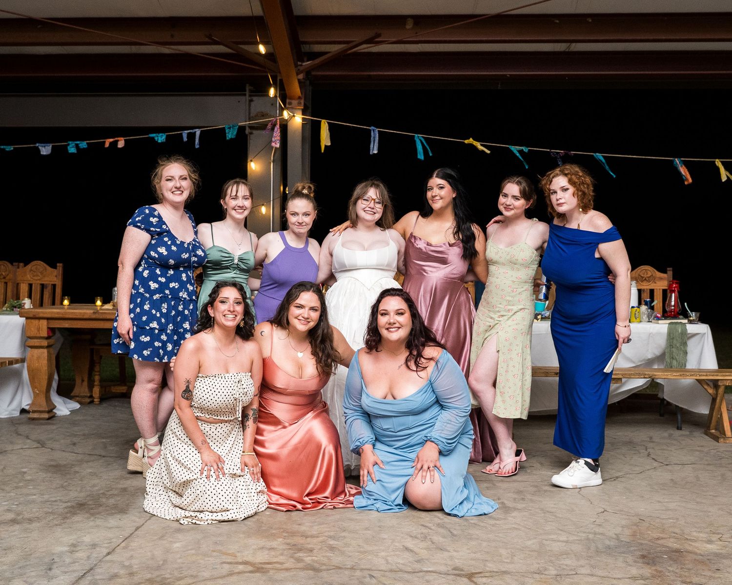 Group of women in formal dresses posing together at an indoor wedding reception celebration.