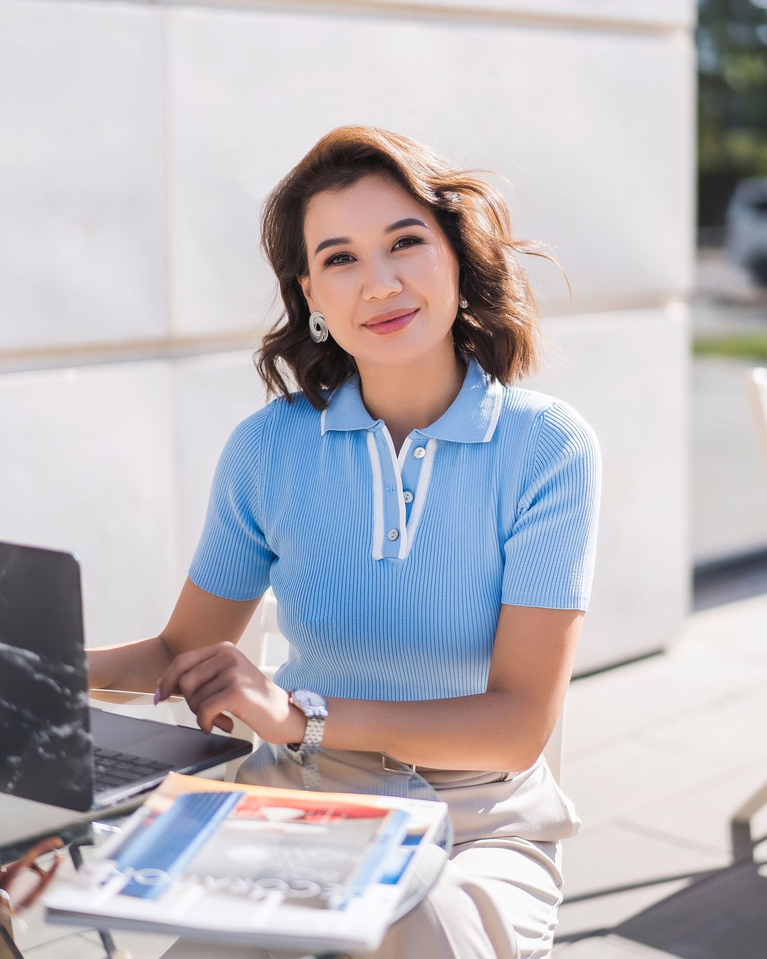 Person in light blue crop top sitting at outdoor table with laptop and papers.
