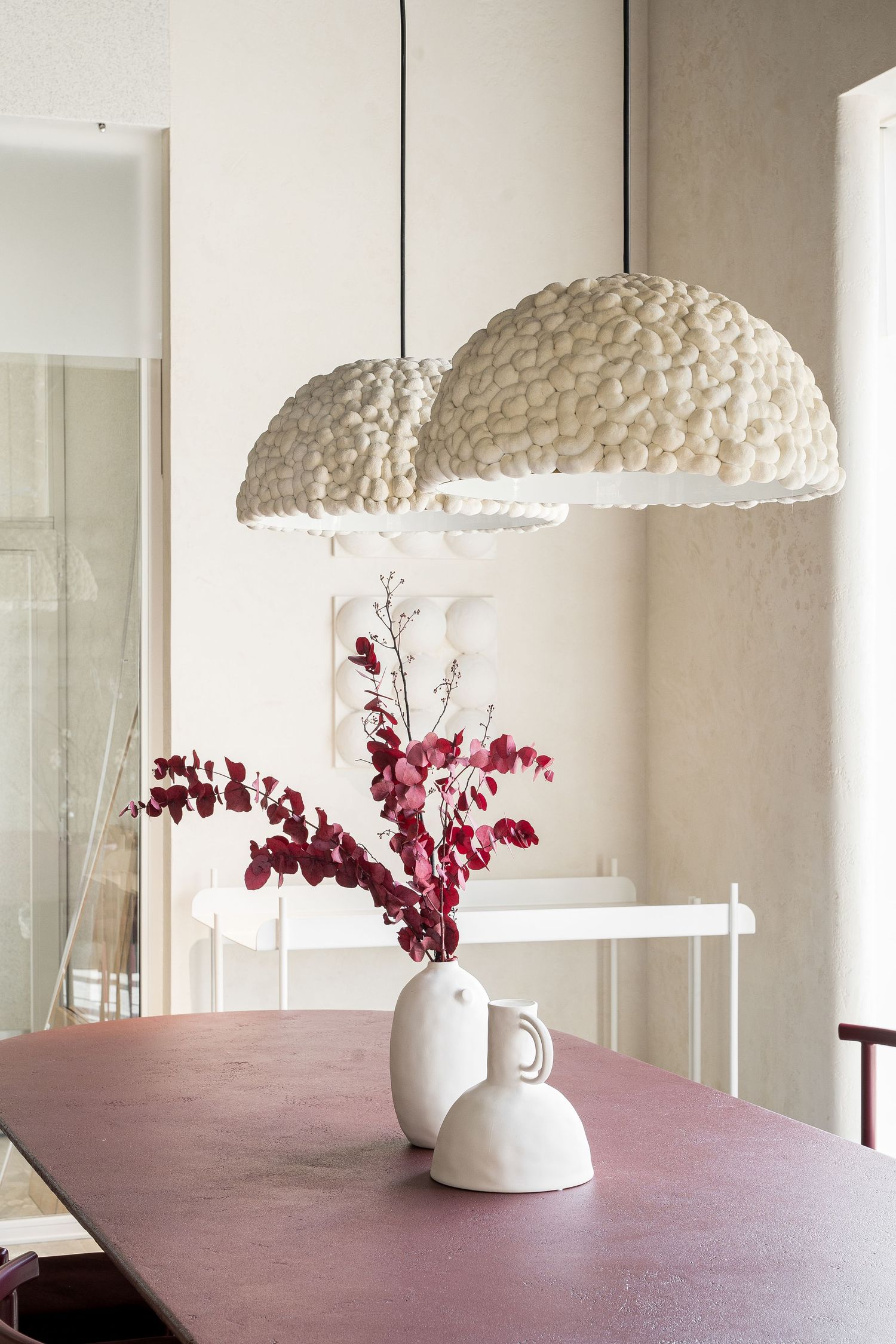 White textured pendant lamps hanging over burgundy tables with red floral arrangements.