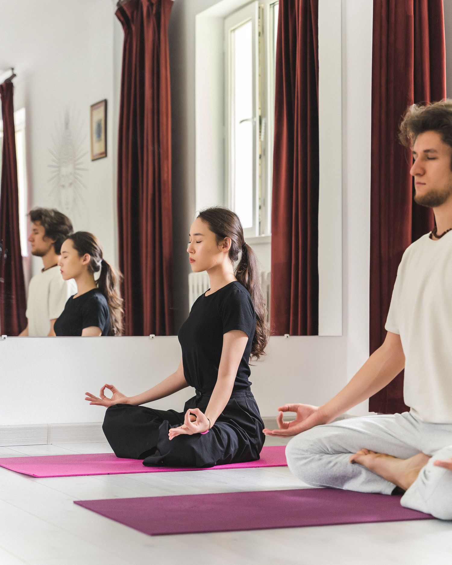 Group practicing yoga and stretching exercises on purple mats in studio with red curtains.