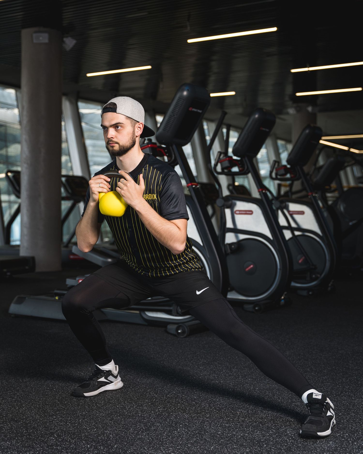 Fitness enthusiast performing lunges with kettlebell in dark gym setting.