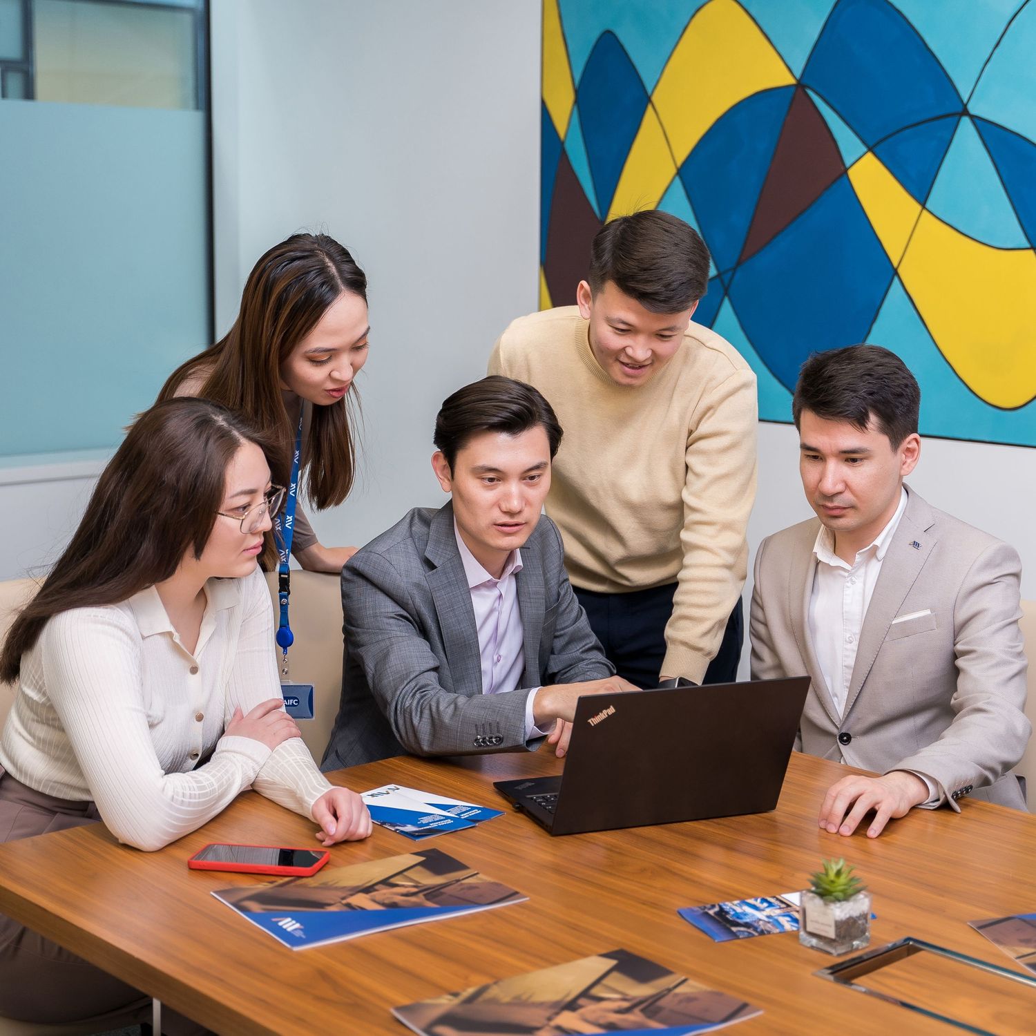 Business team collaborating around a laptop in a modern office with colorful wall art.