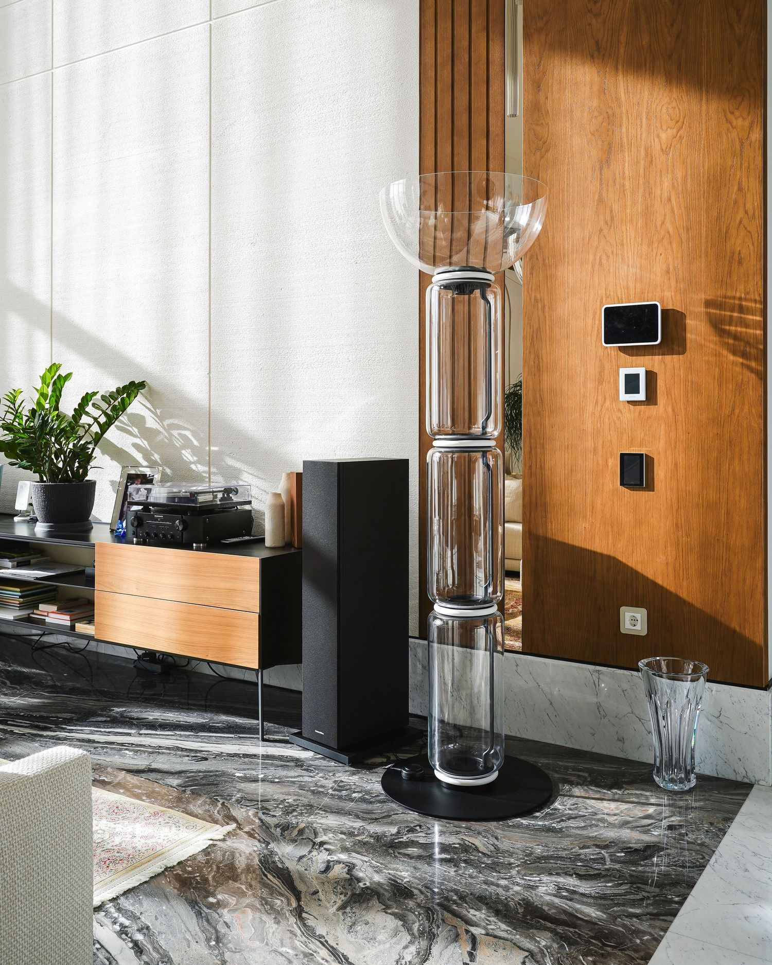 Contemporary living space with wooden panels and black audio equipment on marble flooring.
