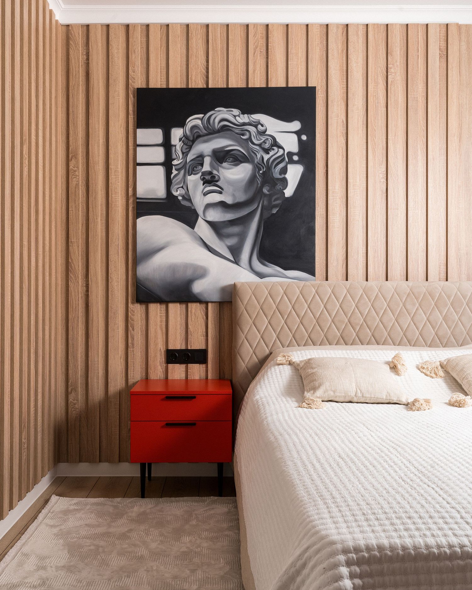 Modern bedroom featuring vertical wood paneling, red nightstands, and dramatic black and white wall art.