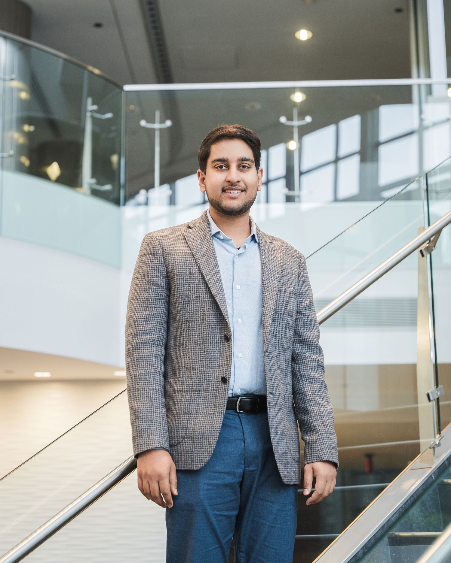 Professional in grey suit standing by modern office staircase.