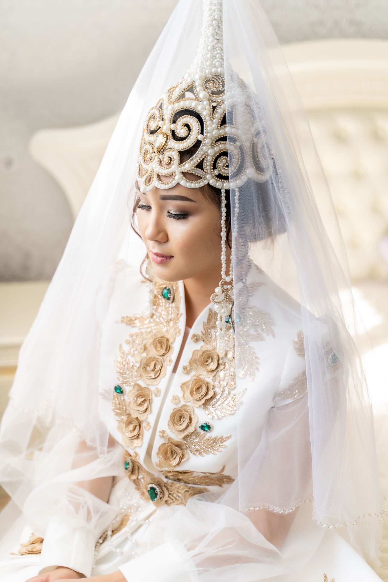Kazakh bride in traditional white and gold embroidered wedding dress with decorative saukele headdress and sheer veil.