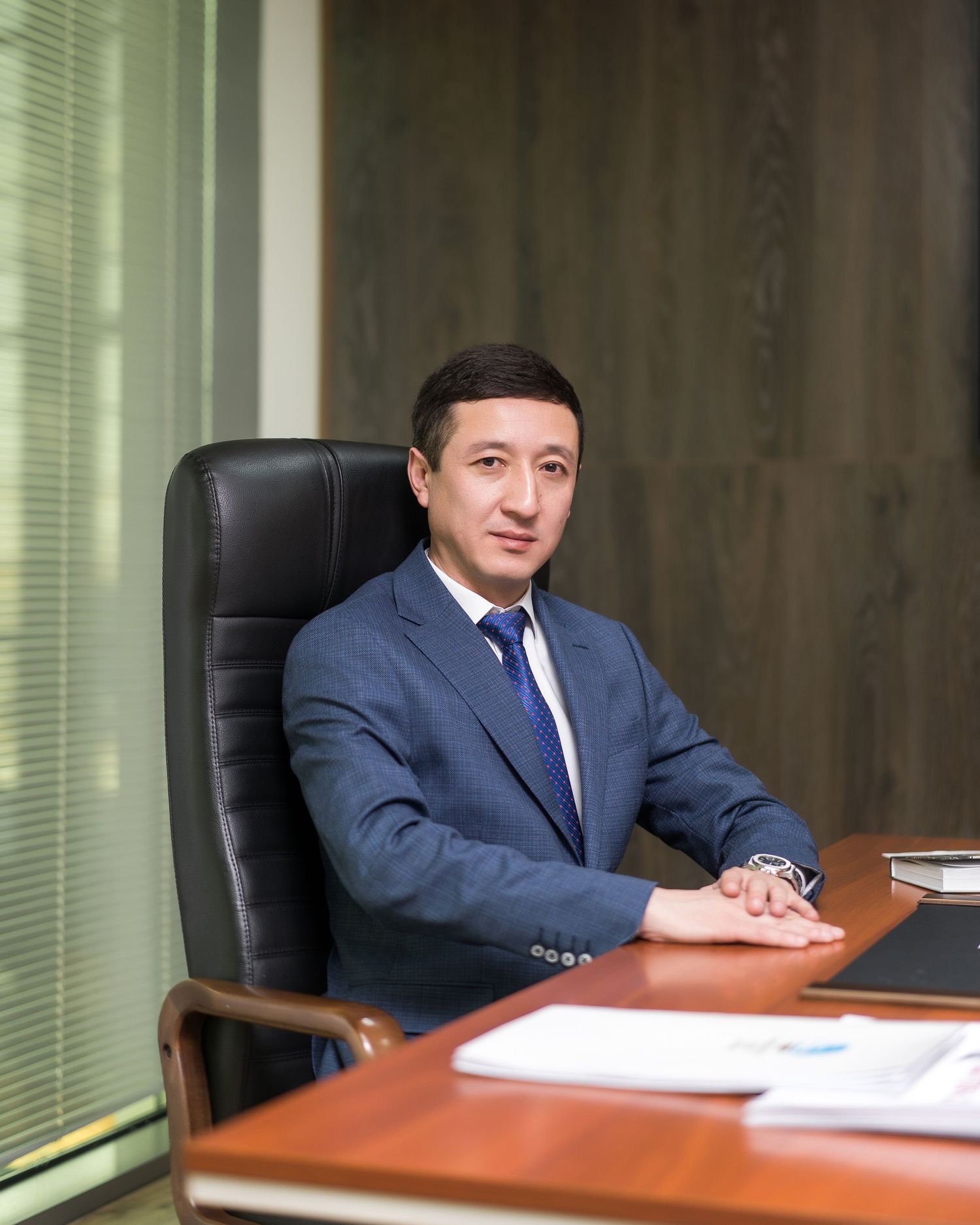 Executive seated at conference room table in navy suit during business meeting.