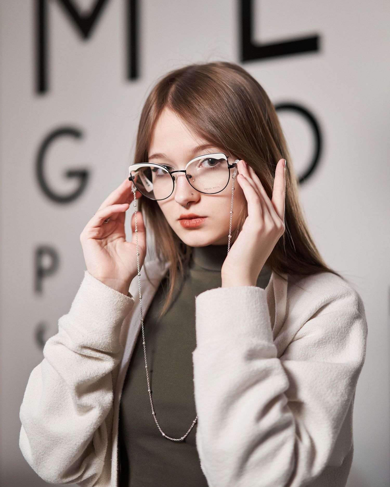 Studio portrait series showing someone adjusting glasses against a grey background with eye chart.