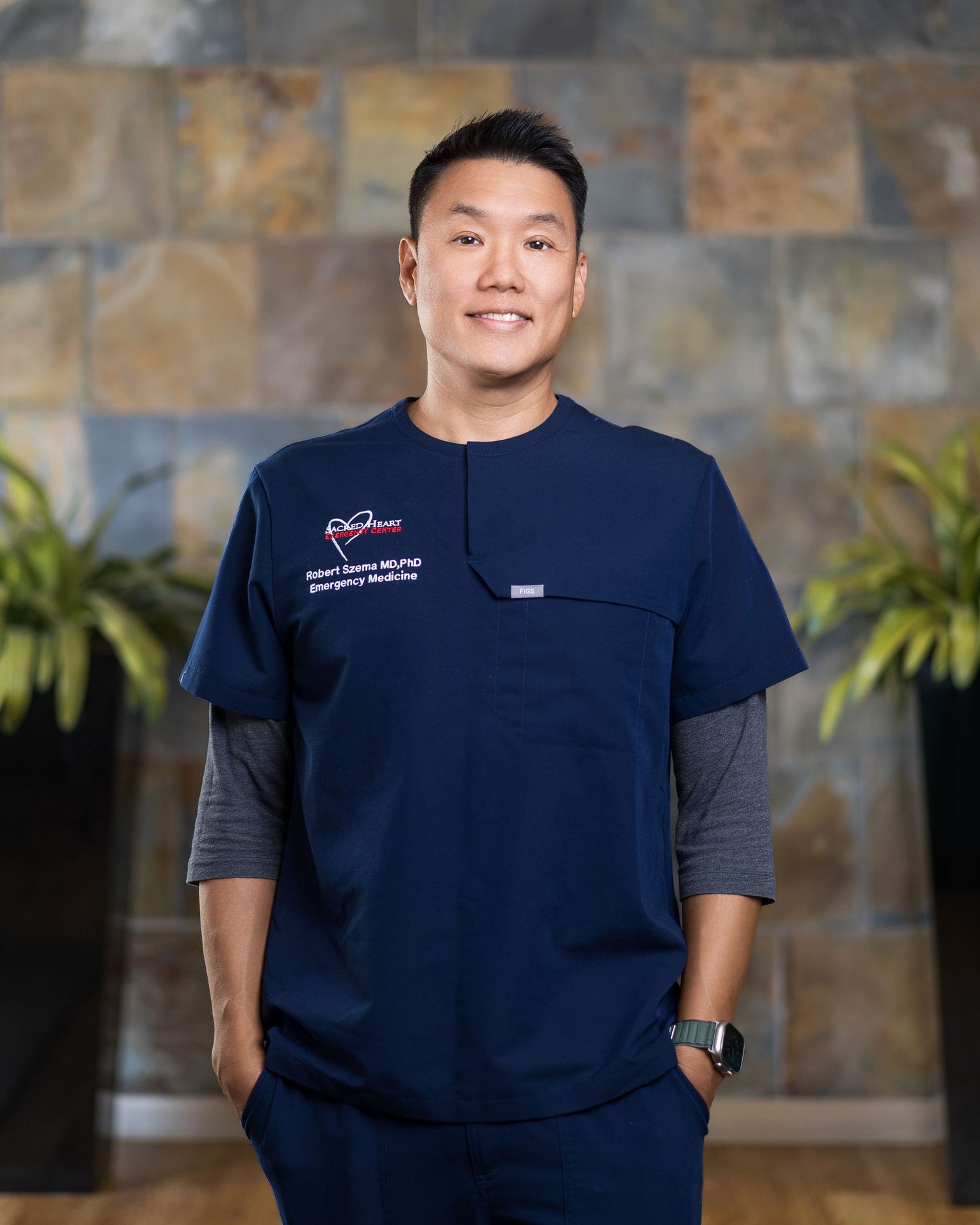 Medical staff member wearing navy blue scrubs against stone wall.
