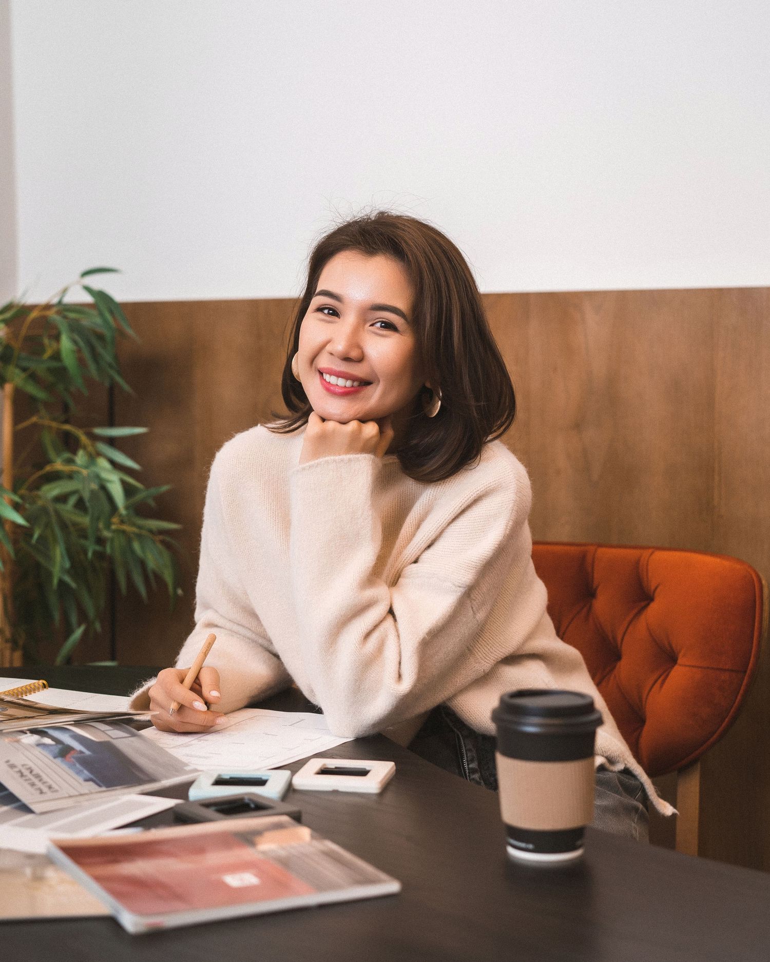 Person in cream sweater relaxing at coffee shop with magazines and drinks.