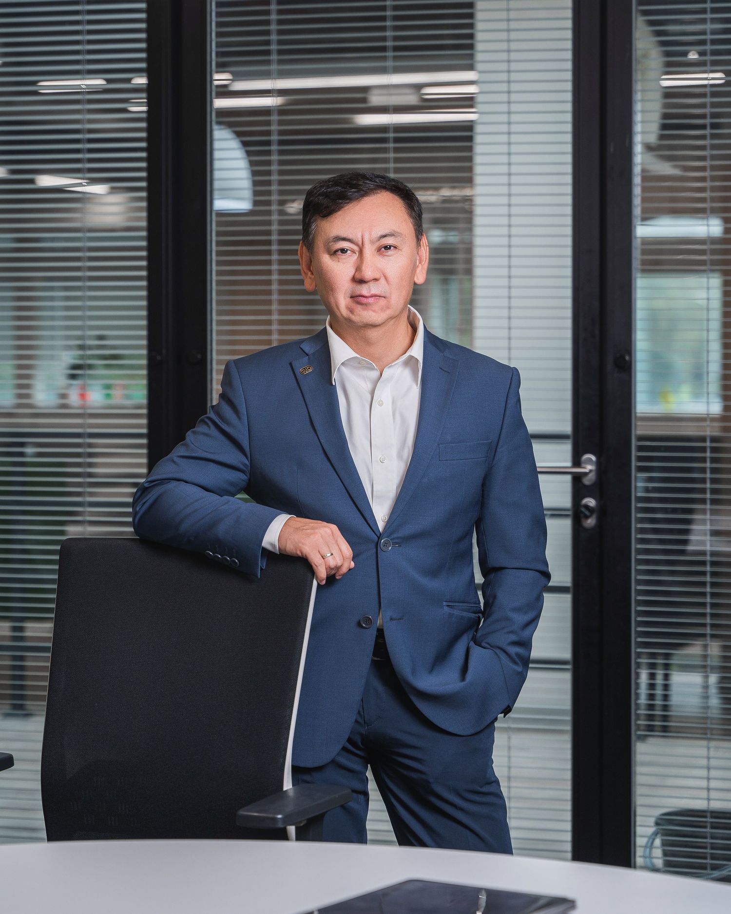 Business executive in navy suit standing in modern office with glass walls.