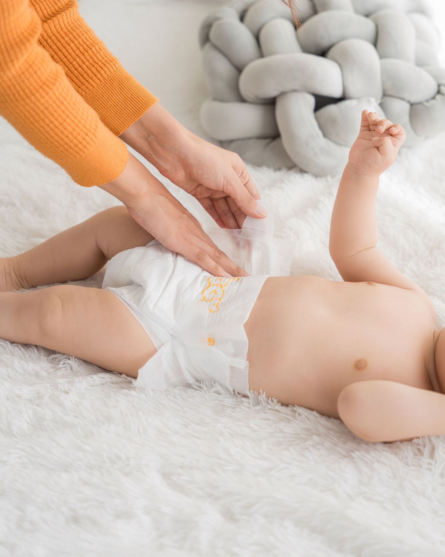 Hands changing baby's diaper on white fluffy surface with gentle care.