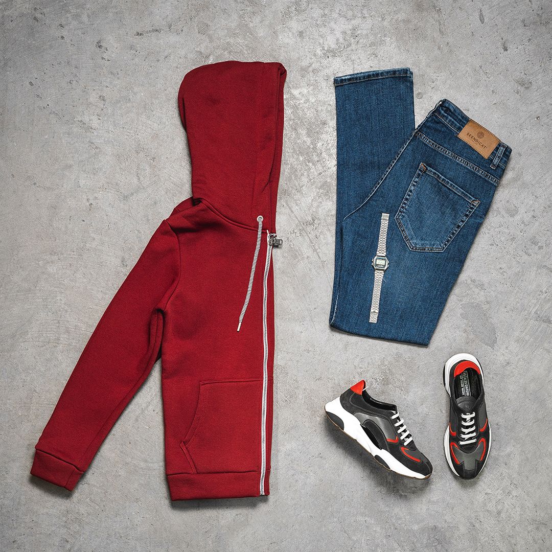 Red sweatpants and blue jeans with sneakers laid flat on concrete surface.