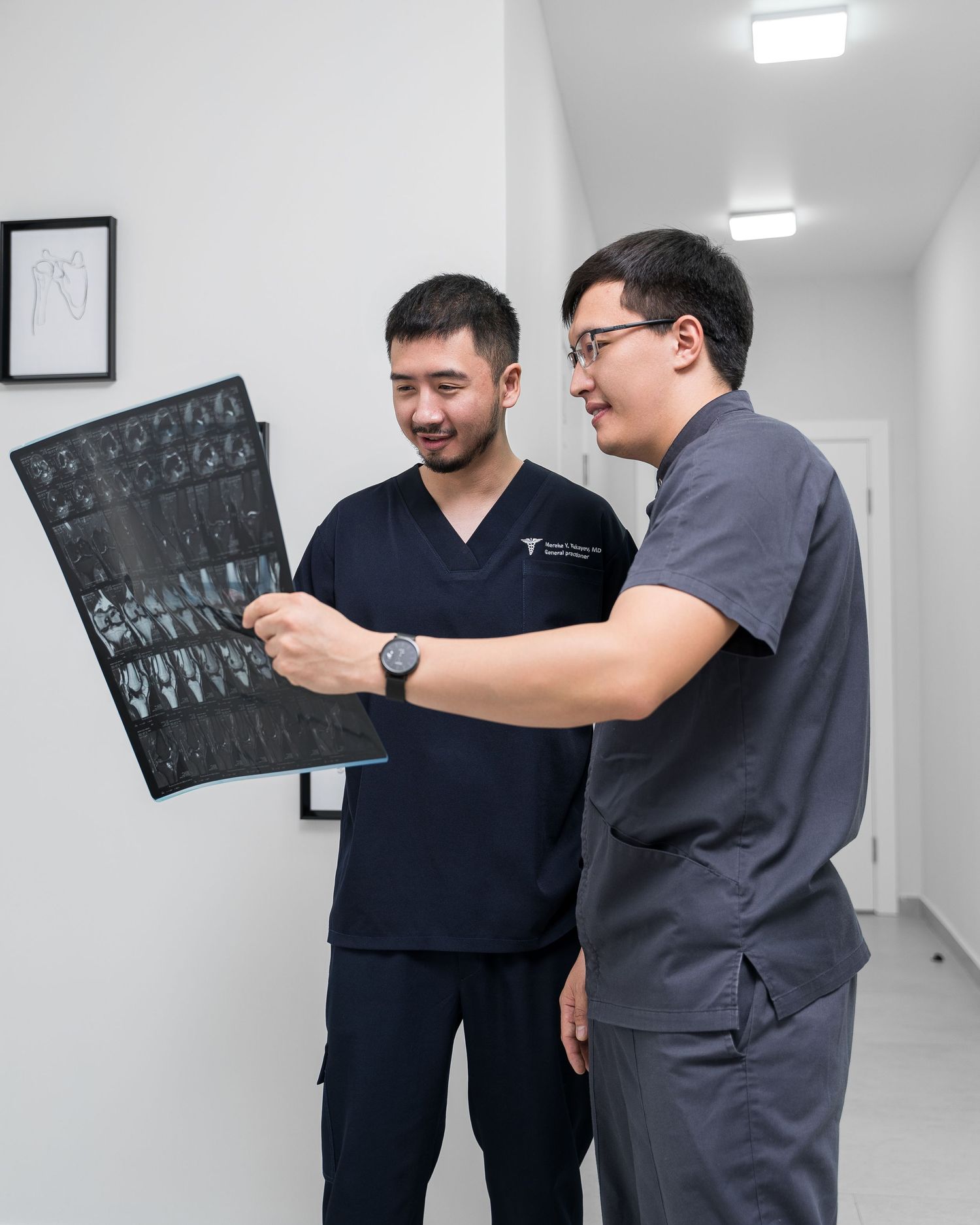 Two medical professionals in scrubs reviewing an X-ray scan in a hospital corridor.