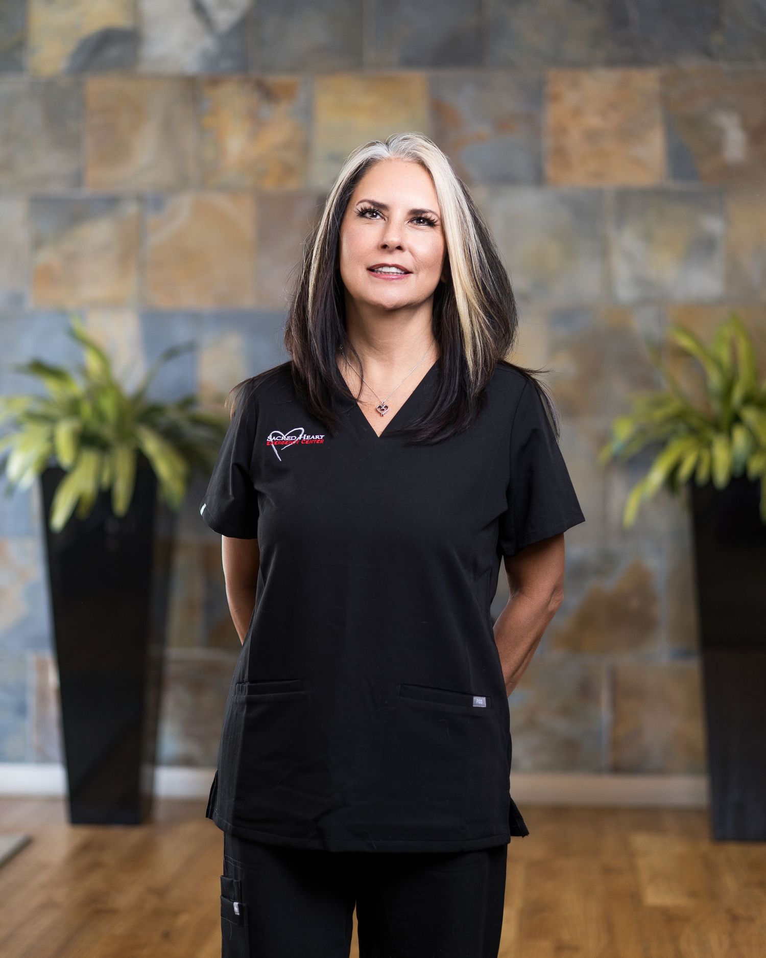 Healthcare professional in black scrubs standing against stone wall background.