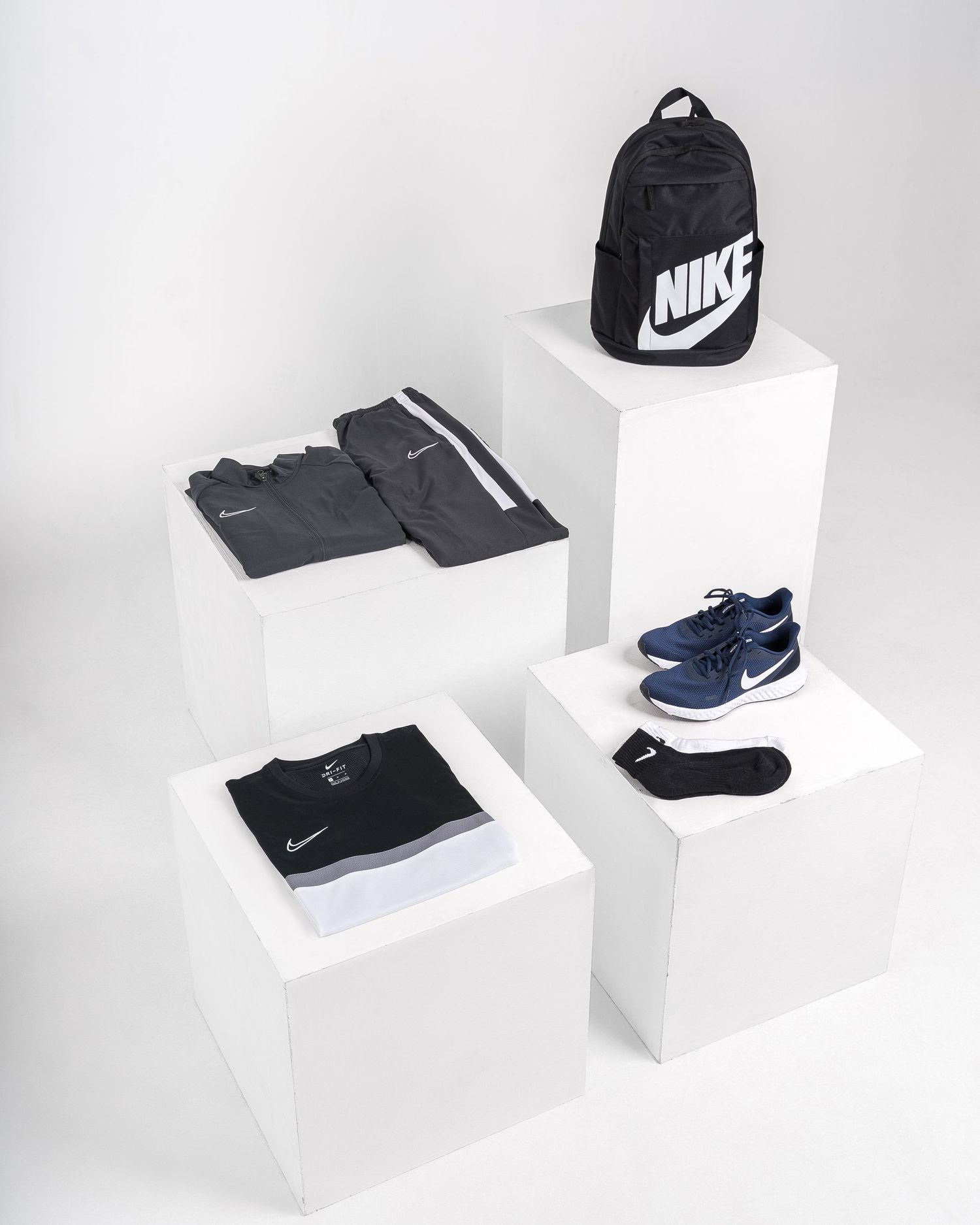 Nike athletic accessories and shoes displayed on white geometric platforms.