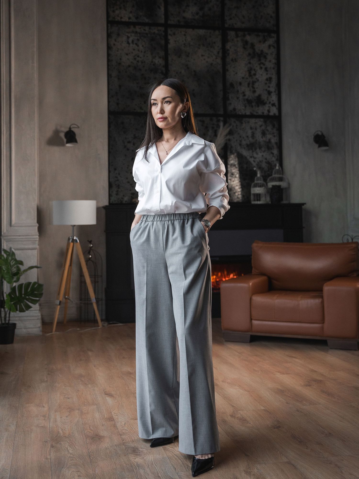 Fashion forward business look featuring white shirt and wide grey pants in modern interior.
