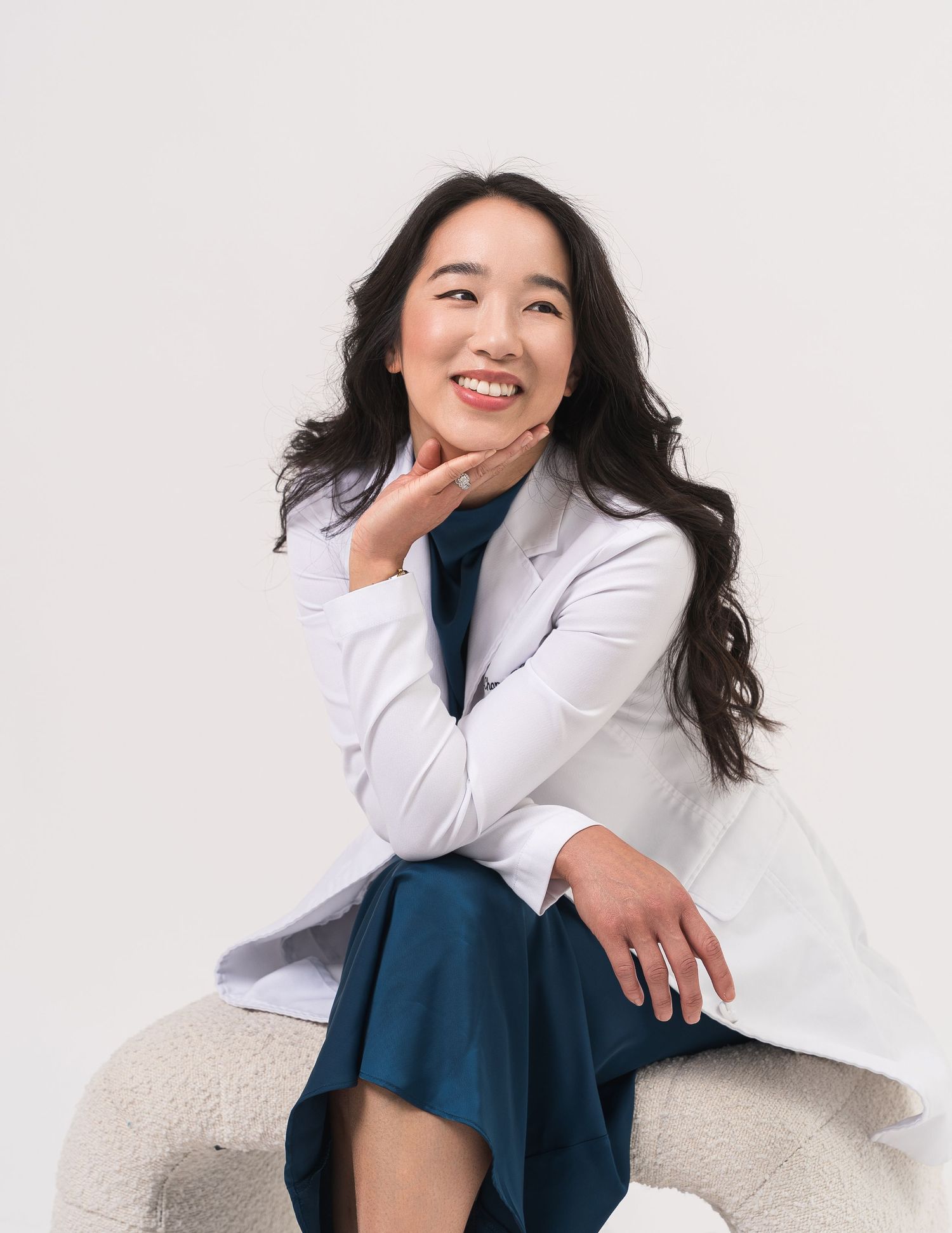 Professional in white coat and blue dress seated on light colored furniture.