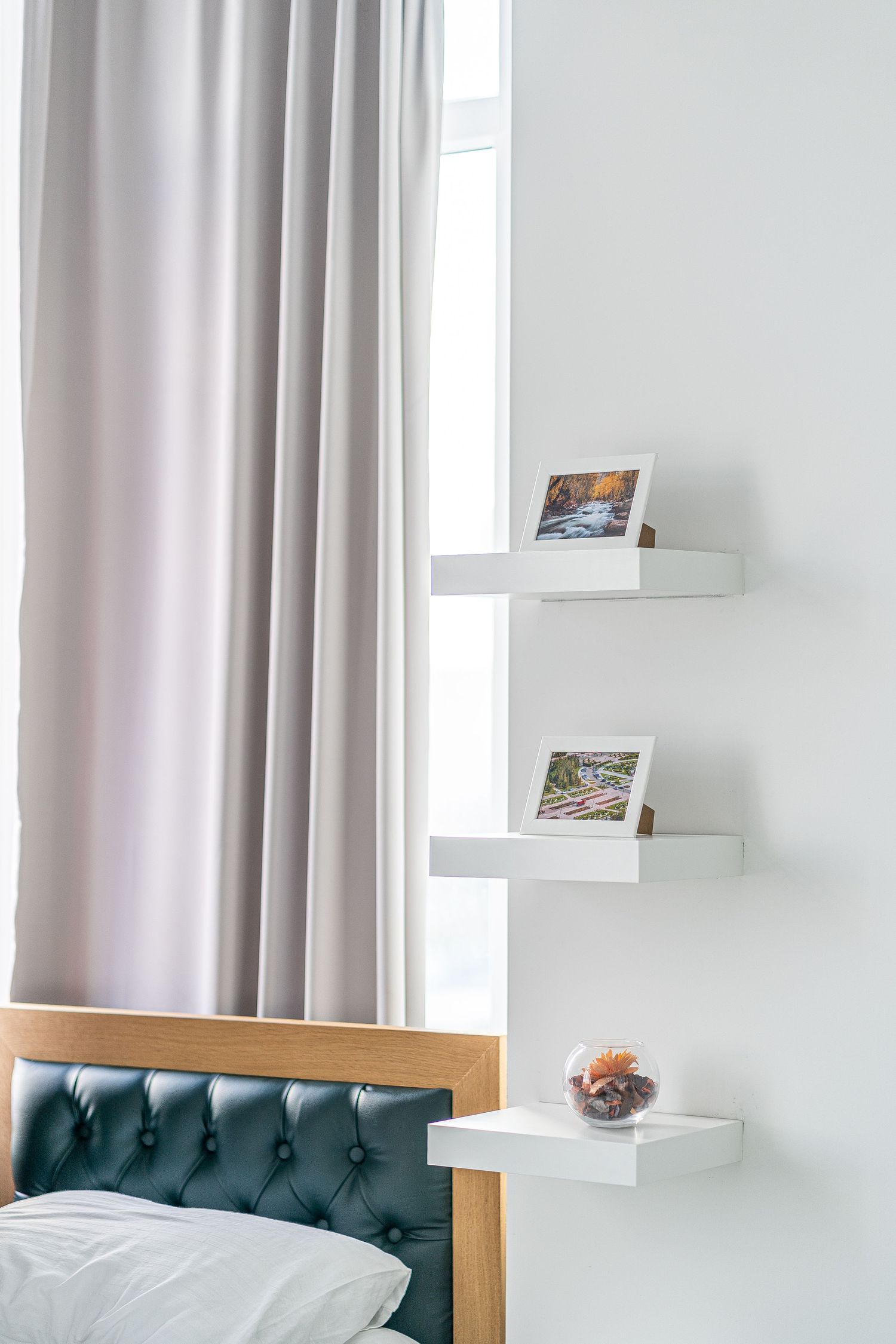 Modern hotel bedroom with teal tufted headboard, white bedding, and natural light from large windows.