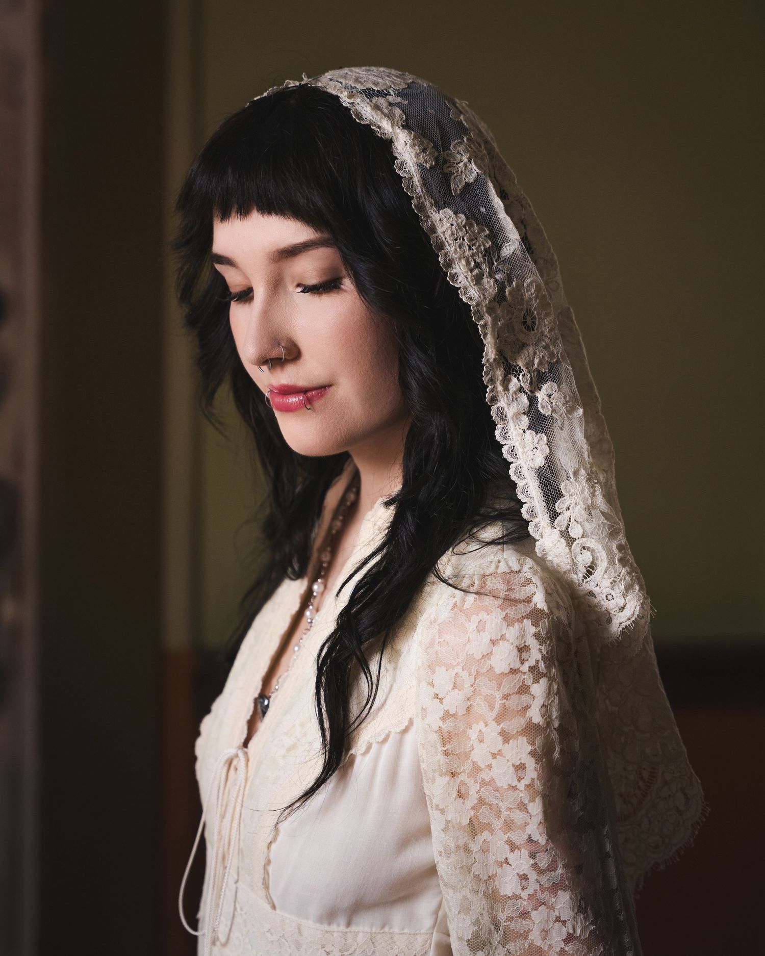 Bride in vintage lace dress and floral veil with eyes closed in elegant portrait.