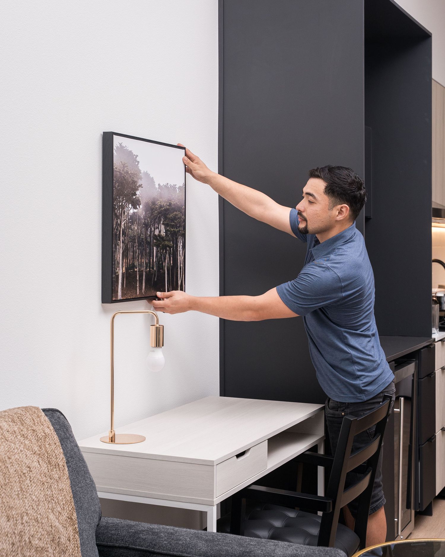 Worker in blue uniform installing artwork on white office walls.