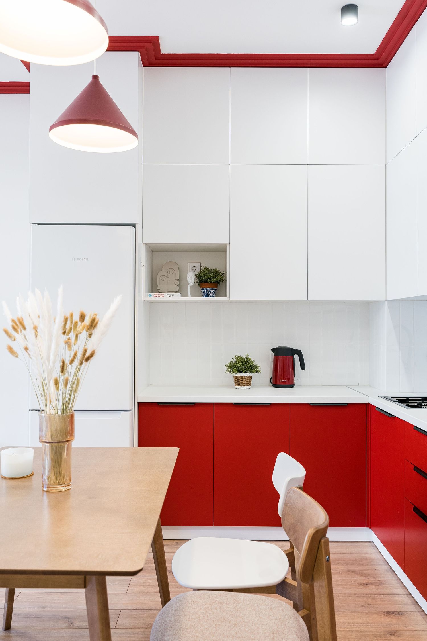 Minimalist kitchen design with red lower cabinets, white upper cabinets, and wooden dining furniture.
