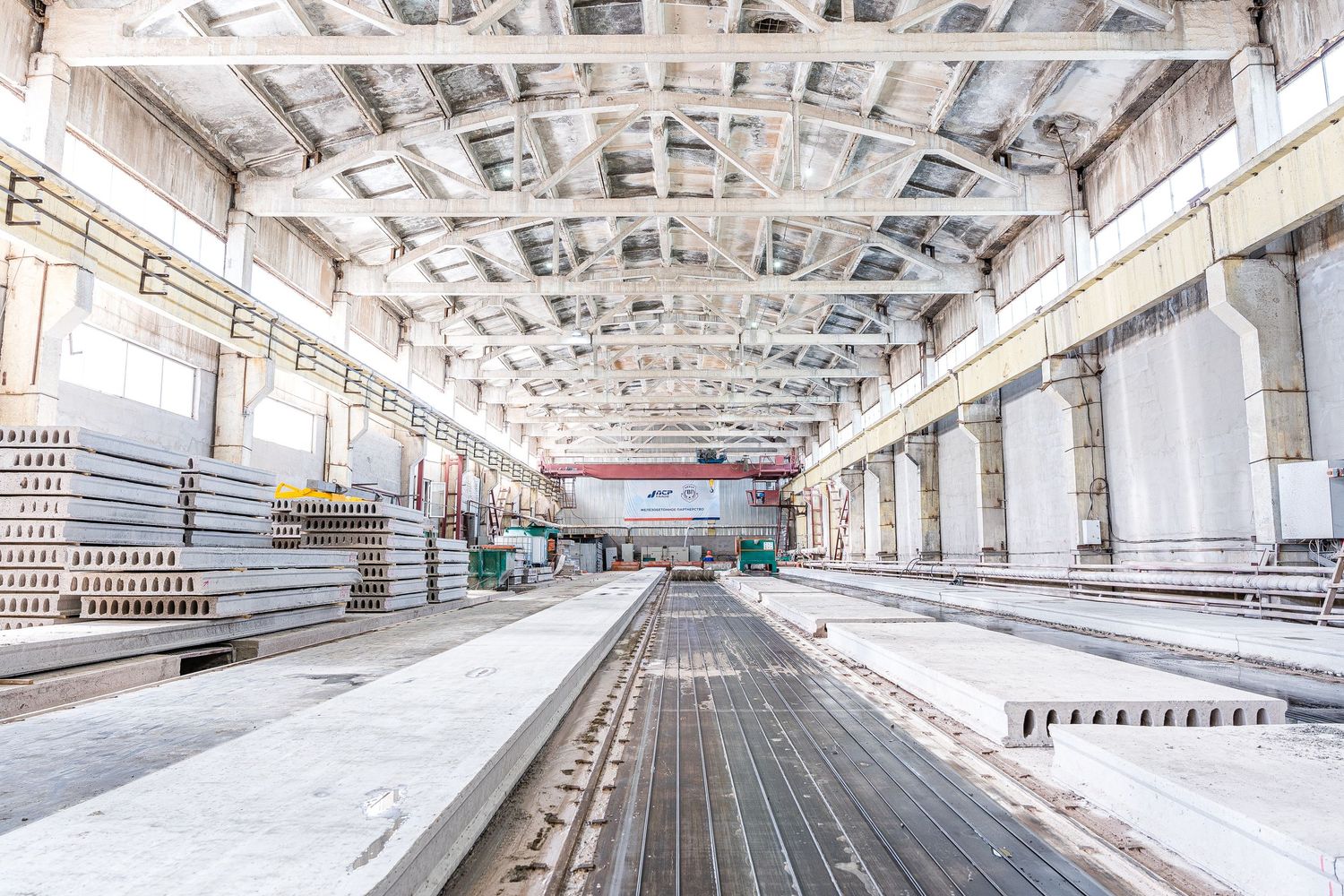 Empty industrial warehouse interior with white ceiling and concrete floor showing long tracks and storage areas.