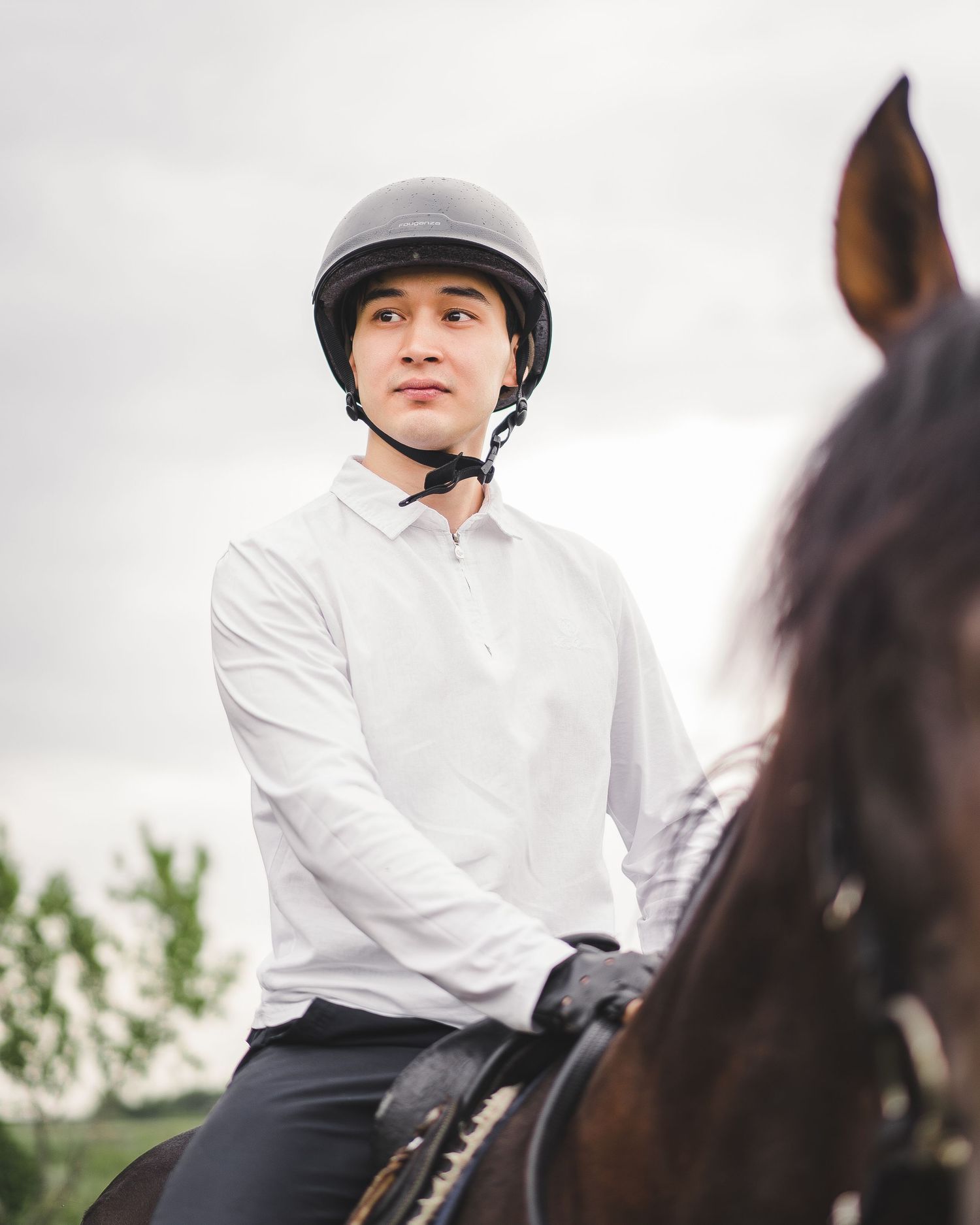 Equestrian wearing white shirt and helmet riding horseback.