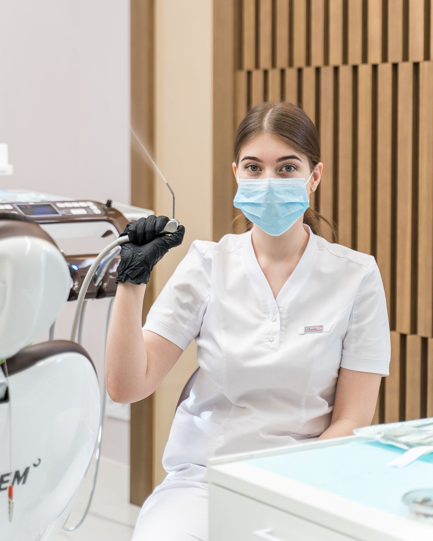 Dental professional in white uniform and mask working at modern clinic reception desk.