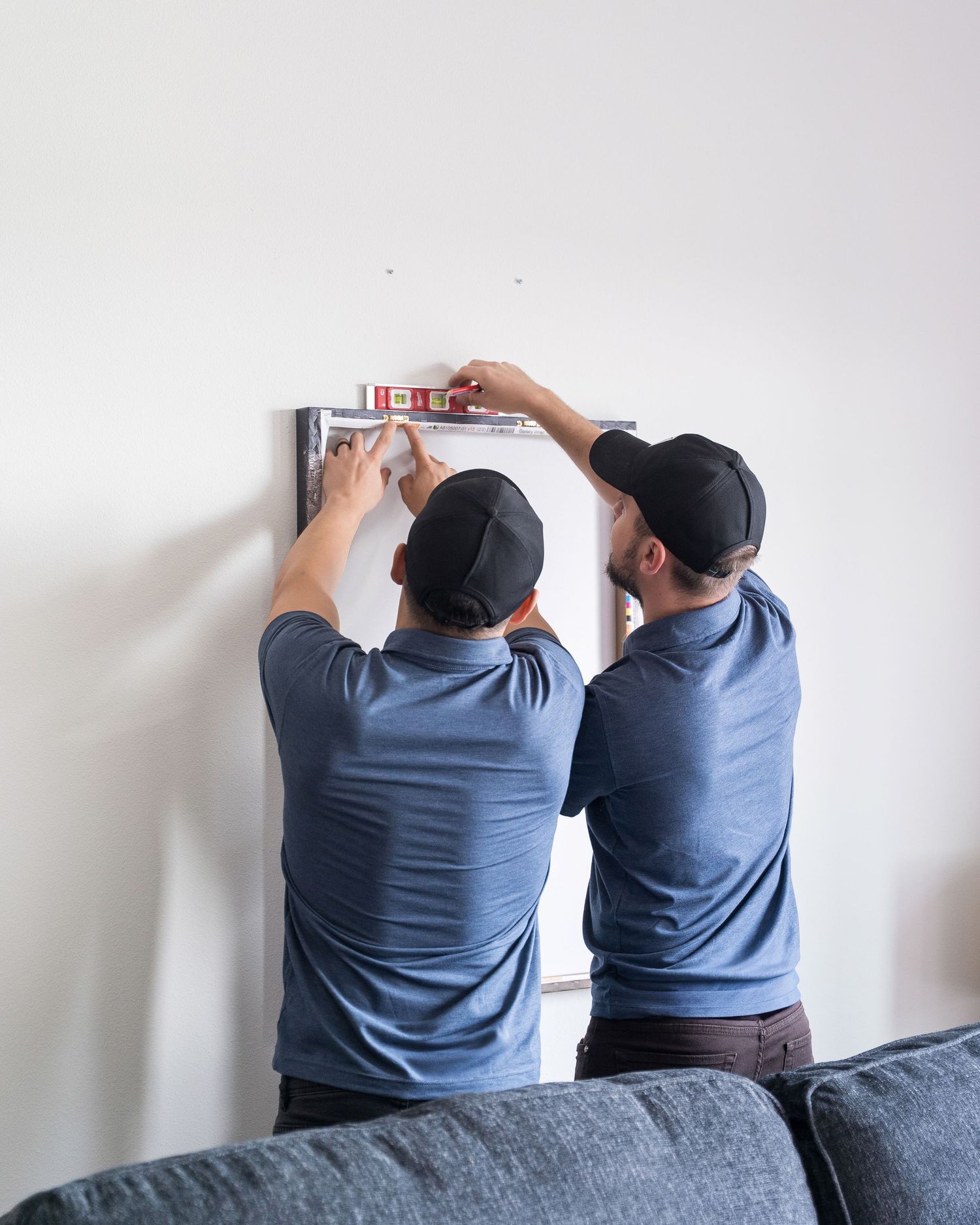 Two maintenance workers in blue uniforms installing equipment on a white wall.