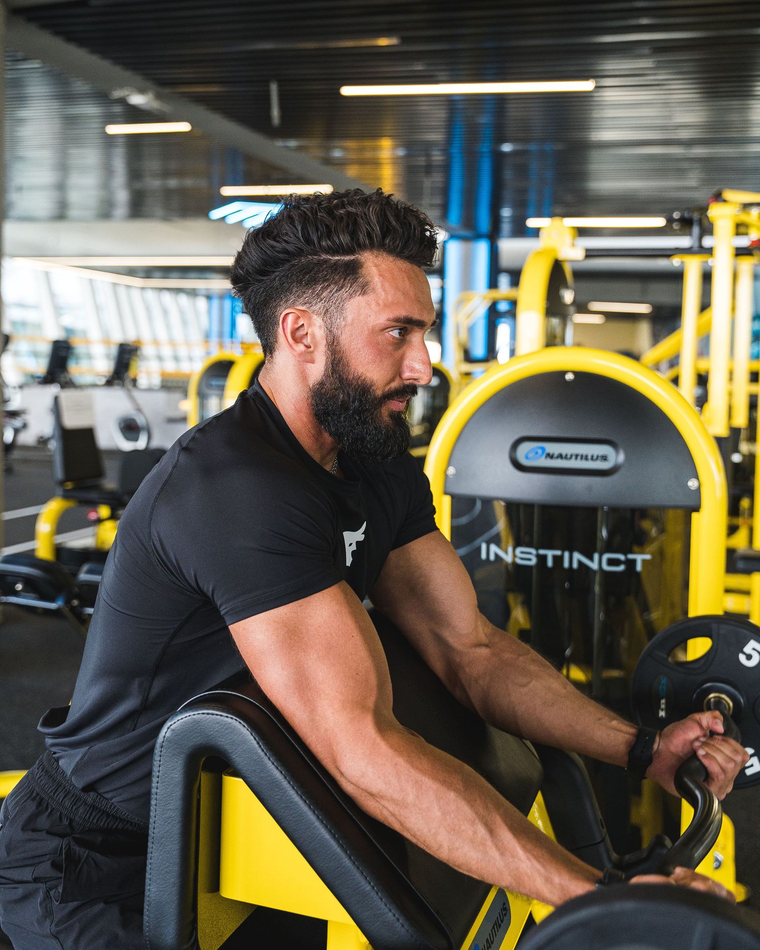 Person working out on exercise equipment in a modern gym with yellow fitness machines.